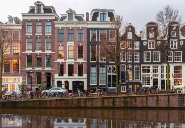 Gün batımında şehrin seddini ve ortaçağ peri evlerinin cephelerini gösteren resimli bir manzara. Amsterdam mı? Hollanda.