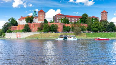 Güneşli bir günde nehrin kıyısındaki kale duvarının arkasındaki eski şehrin binaları ve kuleleri. Krakow. Polonya..