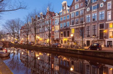 Gün batımında şehrin seddini ve ortaçağ peri evlerinin cephelerini gösteren resimli bir manzara. Amsterdam mı? Hollanda.