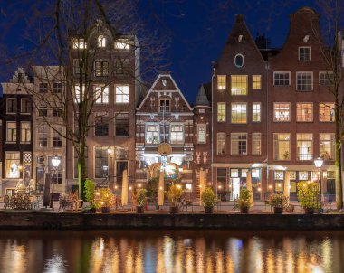 Gün batımında şehrin seddini ve ortaçağ peri evlerinin cephelerini gösteren resimli bir manzara. Amsterdam mı? Hollanda.