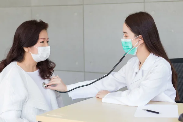 亚洲专业女医生在医院使用听诊器检查老年妇女的肺和心脏健康状况或诊断症状 同时两人都戴着口罩 — 图库照片