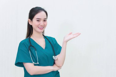 Mavi üniformalı güzel, genç Asyalı kadın doktor beyaz arka plandaki tepeyi gösterip gülümsüyor..