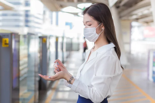 年轻的亚洲女人正在户外车站等火车 同时还要去办公室工作 她喷酒洗手 并戴上医疗面罩作为医疗保健和新的正常生活方式 — 图库照片
