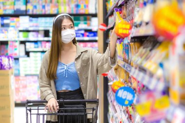 Altın sarısı uzun saçlı genç Asyalı kadın hafta sonu süpermarkete alışverişe giderken COVID-19 'u yeni normal konseptiyle korumak için tıbbi maske takıyor..