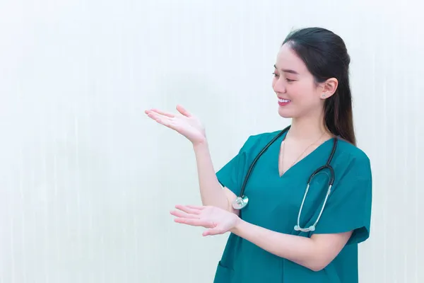 身穿绿色制服的亚洲专业女医生站在那里笑着 同时指着白底的顶部 — 图库照片