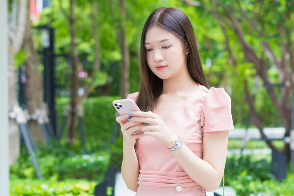 Young Asian professional  business female with long hair is smiling in the garden while looking at the smartphone in her hand, work from anywhere concept.