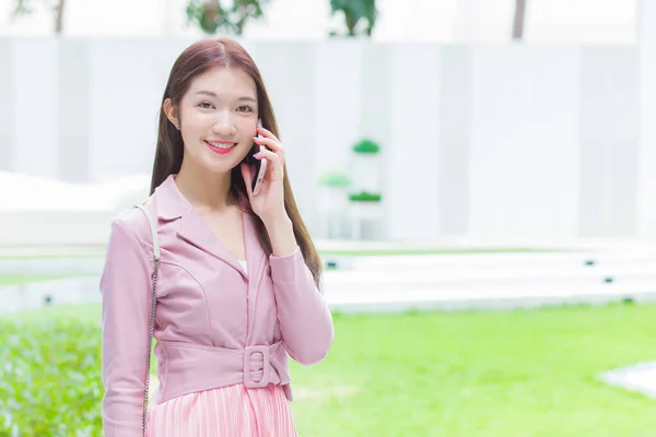 ピンクのドレスの若いアジアのビジネスの専門家は カメラを見て真剣にオフィスビルの誰かと電話をかけています — ストック写真