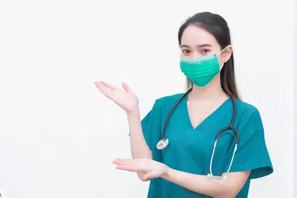 アジアの女性は 白い背景に何かを提案するために彼女の手を示している間コロナウイルス病2019 Covid の発生を保護するために緑の医療服や医療面マスクを着ています — ストック写真