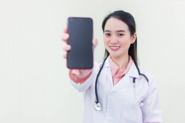 Beyaz sağlık önlüğü ve steteskop giyen güzel Asyalı doktor bir şey sunmak için akıllı telefon gösterisi gösteriyor..