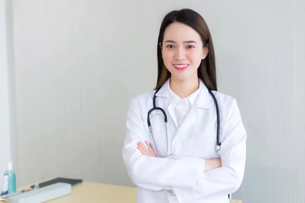 白いローブと聴診器を身に着けているプロのアジア女性医師腕を組んで立って病院の診察室で幸せと笑顔を越えました — ストック写真