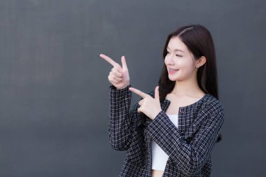 Diş teli takan siyah takım elbiseli Asyalı profesyonel bir kadın koyu gri duvarda bir şey göstermek için işaret ediyor..