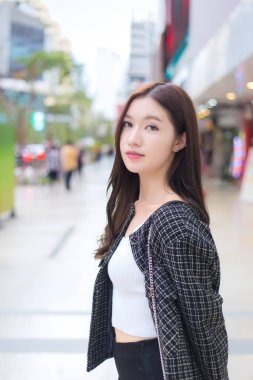 Uzun saçlı, güzel bir Asyalı kadının portresi. Siyah desenli bir ceket giymiş, diş telleri takmış, şehirde yürüyor ve gülümsüyor..
