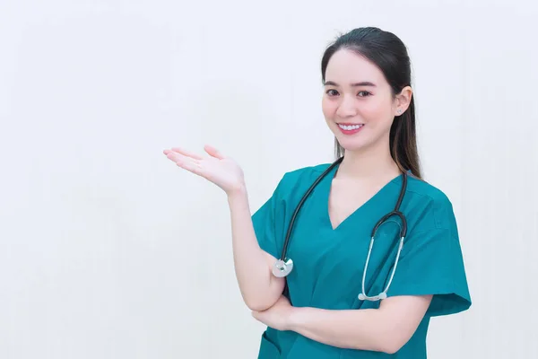 身穿绿色制服的亚洲专业女医生站在那里 微笑着指着白底 — 图库照片