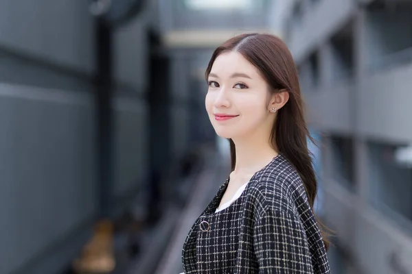 Portrait of a beautiful, long-haired Asian woman side face in a black pattern coat with braces on teeth standing and smiling outdoors in the city.