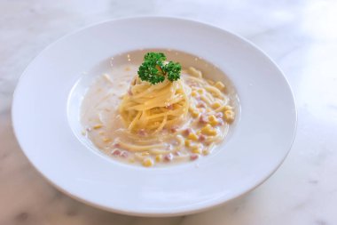 Jambon ve mısır kremi soslu spagetti arka plan olarak mermer masanın üzerine beyaz bir tabak koyun..