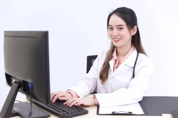 アジアの女性医師がキーボードを入力してコンピュータに情報を記録している彼女は病院で医療面マスクを身に着けている間 — ストック写真