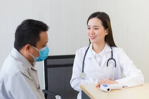 亚洲漂亮的年轻女医生一边戴上口罩 一边与一位男性病人谈论他的疼痛和症状 以防止科罗纳韦勒斯病和温度计在医院的桌上出现 — 图库照片
