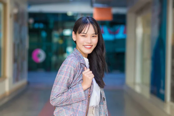 Confident professional young Asian business woman who wears a brown striped blazer and shoulder bag smiles happily and looks at the camera as she commute to work through the old town.