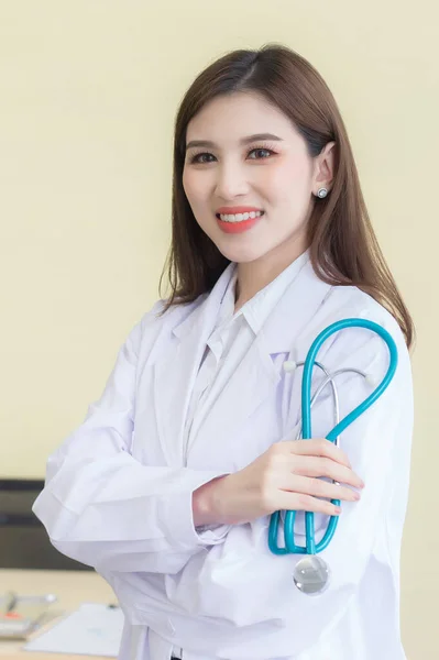 若い美しいアジアの女性医師腕を組んで立って病院で幸せと笑顔を越えました 白い衣と聴診器を身に着けて — ストック写真