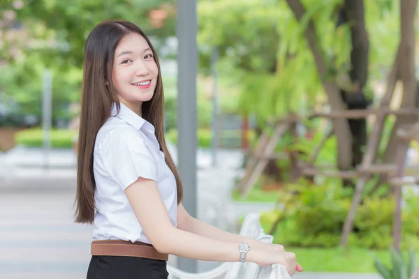 Portrait of an adult Thai student in university student uniform. Asian beautiful girl sitting smiling happily at university with a background of garden trees.