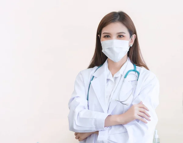 アジア系の女性医師が腕を組んで立っていた 白いローブを着てマスクと聴診器をつけて — ストック写真