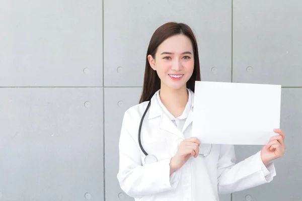 医療の概念に何かを提示する白い紙を保持し 示す医療コートを身に着けているアジアの女性医師 — ストック写真