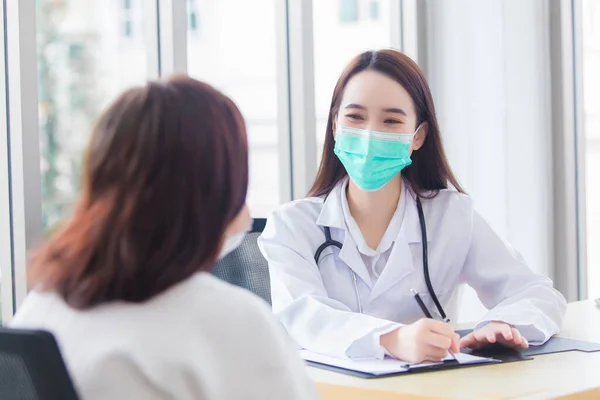 Asian elder female consults with professional woman doctor about her symptom or health problem while she wears medical face mask in examination room at hospital at health care,pollution PM2.5,new normal and coronavirus protection concept.