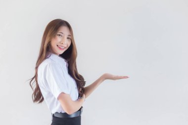 Yetişkin bir Taylandlı öğrencinin üniversite öğrenci üniforması içindeki portresi. Asyalı güzel kız beyaz arka planda kendine güvenen bir şey sunmak için ayakta duruyor..