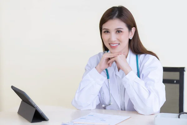 亚洲年轻貌美的专业女医生坐在医院的办公室里 桌上有一个剪贴板和数字平板电脑 — 图库照片