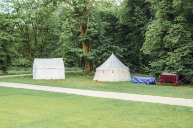 Ormanın arka planında yiyecek ve çadırları olan klasik ortaçağ arabaları. Ortaçağ askeri birliği. Kalenin kenar mahallelerinde çadırlar.