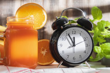 Çalar saat 12: 00 'yi gösteriyor ve bardakta taze sebze suyu var. Bir bardak taze sıkılmış meyve suyu. Kopyalama alanı olan arkaplan
