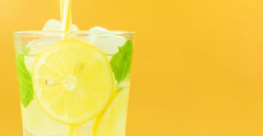 Taze ve soğuk limonlu bir bardak. Sarı arka planda limonata. Limonlu ve naneli mojito kokteyli. Metin için yer