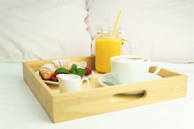 Kahve, portakal suyu ve tahta saplı kruvasan. Beyaz çarşafların üzerinde yatakta romantik bir kahvaltı, pencereden gelen ışık. Arka planda sabahları pencereden gelen sıcak ışık