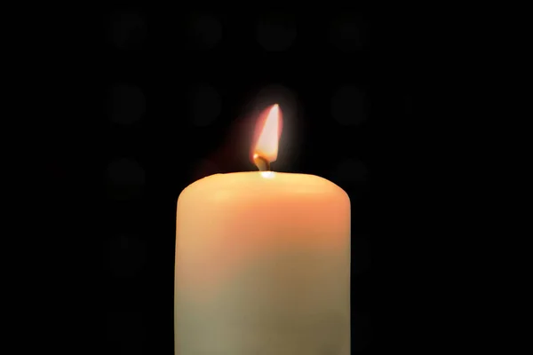 Burning wax candle on a black background. One candle is lit in the dark or against a black background