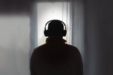 Man In Headphones Looks Out Window. Back View.