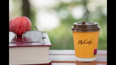 Paper cup with McDonald's coffee on a background of yellow leaves. A glass of coffee on a park bench. Background with copy space