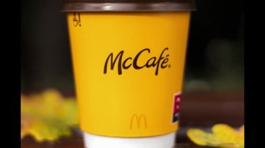 Paper cup with McDonald's coffee on a background of yellow leaves. A glass of coffee on a park bench. Background with copy space