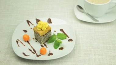 A delicious piece of sponge cake on a white plate. Sweet poppy cake with berries and mint on a plate. Physalis berries. Zooming in, zooming in on the camera
