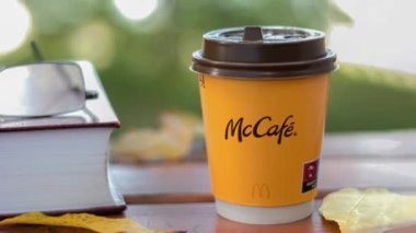 August 16, 2022 - Warsaw, Poland: Coffee in a paper cup over the open sky. A glass of coffee from McDonald's on a background of yellow leaves. Camera zoom. Place for text