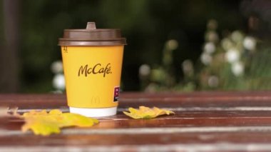 August 16, 2022 - Warsaw, Poland: Coffee in a paper cup over the open sky. A glass of coffee from McDonald's on a background of yellow leaves. Camera zoom. Place for text