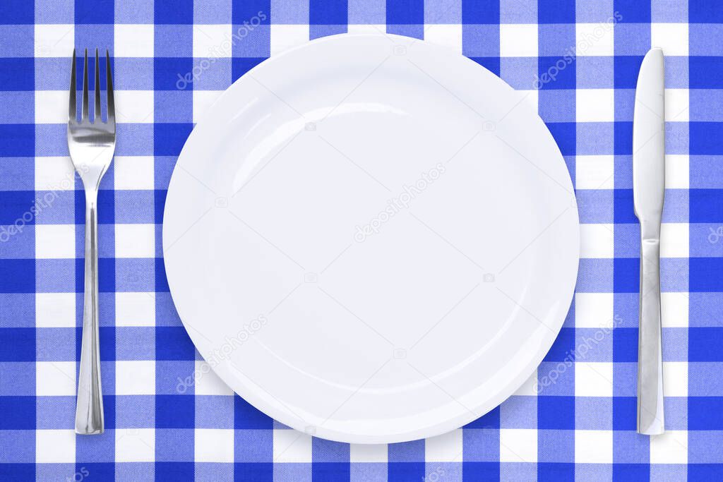 Classic cooking template - top view of an empty white ceramic plate and cutlery on a blue checked tablecloth 