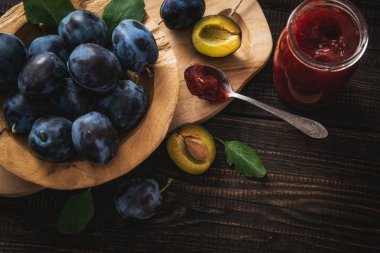 Preparing traditional plum jam at home. Fresh plums in a wooden bowl with jar and spoon on a vintage table.