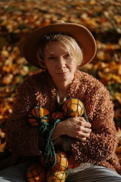 秋の公園で帽子をかぶった若い美しい女性 オレンジの文字列バッグ 女性は秋の葉を投げます 秋の気分 自然の明るい色 — ストック写真