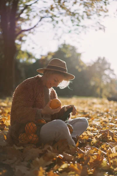 秋の公園で帽子をかぶった若い美しい女性 オレンジの文字列バッグ 女性は秋の葉を投げます 秋の気分 自然の明るい色 — ストック写真