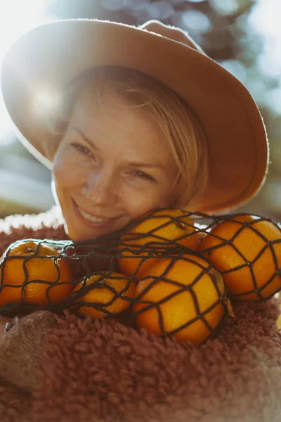 一个年轻美丽的女人 戴着一顶帽子在秋天的公园里 一个带着橙子的绳子袋 一个女人吐着秋天的叶子 秋天的心情 大自然的灿烂色彩 — 图库照片