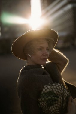 Büyük bir şehrin ortasında kısa saçlı, şapkalı, orta yaşlı güzel bir kadın. Yakın plan portre, yumuşak arka plan ışığı.