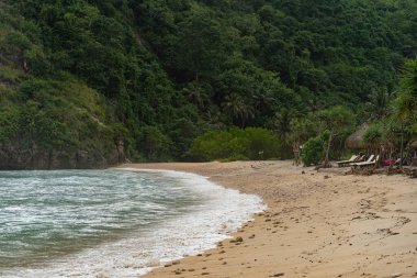 Doğa arka planı, mavi okyanus, kıyıda dalgalar, yemyeşil tropikal bitki örtüsüyle kayalık kenarı
