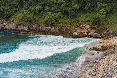 Tropikal bir zemin, mavi suyu olan bir sahil, taşa vuran dalgalar