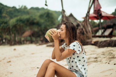 Genç ve güzel bir kadın hindistan cevizi suyu içiyor.