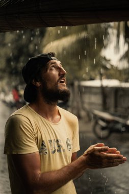 Tropikal yağmurun altında şapkalı yakışıklı genç sakallı adam..
